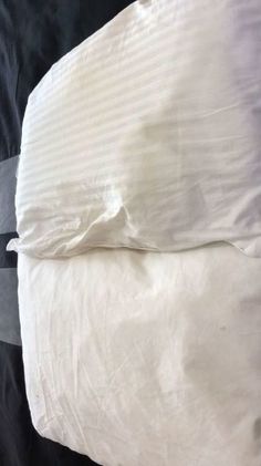 an unmade bed with white sheets and pillows on it's side, in front of a black background