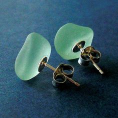 two sea glass studs are sitting on a blue surface with one earring in the shape of a heart