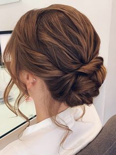 a woman sitting in front of a mirror with her hair pulled into a low bun