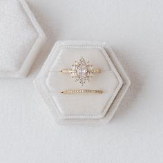 an engagement ring sits on top of a white velvet hexagonal box that holds it