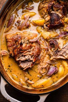 a pot filled with meat and potatoes on top of a wooden table