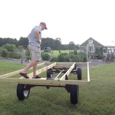 a man is standing on the back of a trailer with wheels attached to it and pulling a cart behind him