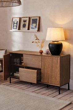 a living room scene with focus on the sideboard and lamp, which has been placed in front of two framed pictures