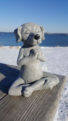 a statue of a dog sitting on top of a wooden bench next to the ocean