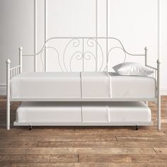 a white metal daybed with two pillows on it's sides and a wooden floor