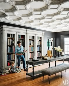 a man standing next to a little boy in a room filled with books and furniture