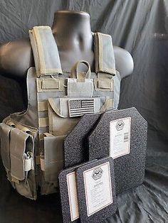 an army vest with two tags attached to it and another item next to it on a mannequin