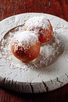 two pastries covered in powdered sugar sit on a white plate atop a wooden table