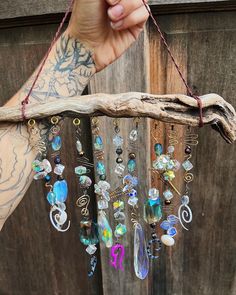 a person holding up a piece of wood with many different colored beads hanging from it