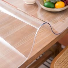 a wooden table topped with a bowl of fruit and a plastic wrapper on top of it