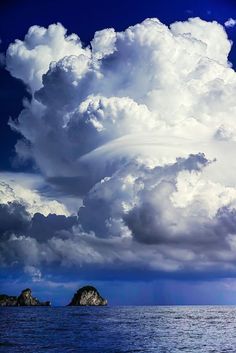 a large cloud is in the sky over some rocks and water with an island in the foreground