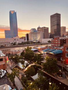 the city skyline is lit up at sunset with tall buildings in the foreground and trees on either side