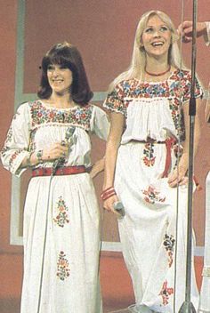 two women standing next to each other in front of a microphone and wearing white dresses