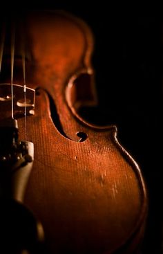 an old violin sitting on top of a wooden table next to a black wall with light coming through the strings