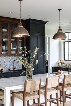 a kitchen with black cabinets and white counter tops, two pendant lights hanging over the island