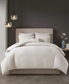 a bed with white linens and pillows in a gray room next to two lamps