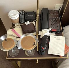 two cups of coffee are sitting on a tray next to a phone and other items