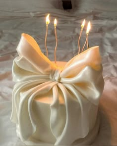 a white cake with three candles in it and a bow on the top is sitting on a table