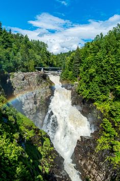 a waterfall in the middle of a forest with a rainbow above it on a sunny day