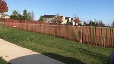 a fence that is next to a sidewalk in front of some houses with trees on the other side