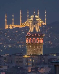 a large building with many lights on it's sides and some buildings in the background