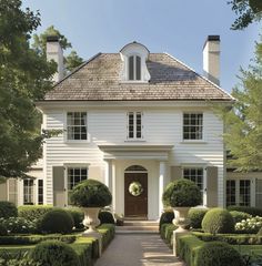 a large white house with hedges around the front door and entry way leading to it