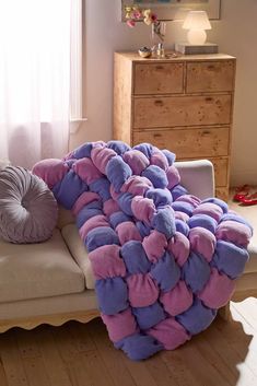 a purple and pink blanket sitting on top of a white couch next to a window