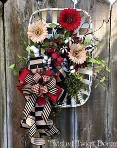 a wreath hanging on the side of a wooden fence with flowers and ribbons attached to it