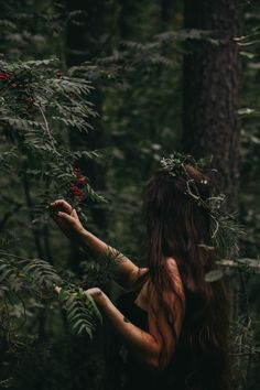 a woman with long hair standing in the woods holding berries on her hand and wearing a wreath around her head