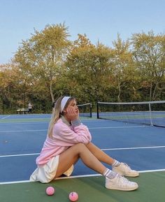 a woman sitting on the ground with tennis balls in front of her and trees behind her