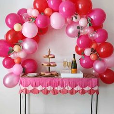 a table topped with lots of pink and red balloons next to a wine glass filled bottle