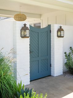 a blue door with two hanging lanterns on it's side next to some plants