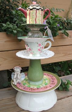 three tiered cake stand with cupcakes and teacups on it in front of a wooden bench