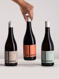 three wine bottles with labels on them being held by a hand