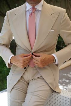 a man in a tan suit and pink tie is sitting on a white bench with his hands behind his back