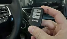 a person holding a remote control in their hand next to a steering wheel and dashboard