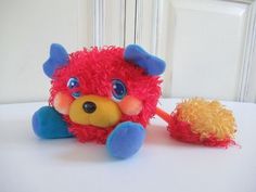 a stuffed animal with blue eyes and red hair sitting on a white table next to a yellow ball