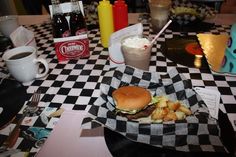 a hamburger and fries are on a checkered tablecloth with cups of sodas