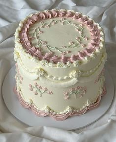 a three layer cake with pink and white frosting on a tablecloth covered surface