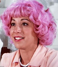 a woman with pink hair is smiling at the camera