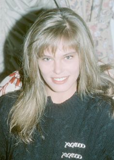 a woman with long blonde hair wearing a black shirt and smiling at the camera while sitting on a couch