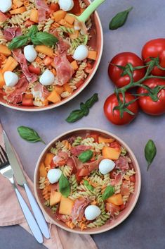 two bowls filled with pasta and vegetables on top of a table next to silverware