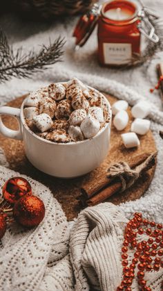 a cup of hot chocolate with marshmallows and cinnamon on a tray next to christmas decorations