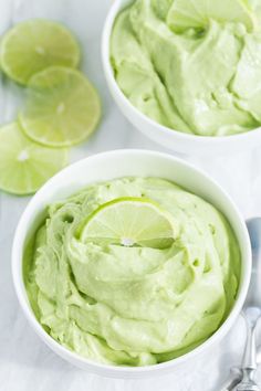 two white bowls filled with guacamole and lime wedges on the side