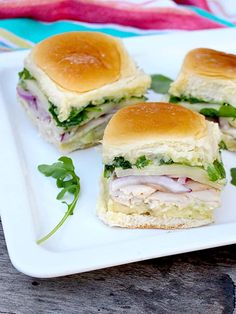 three sandwiches cut in half on a white plate with green garnish and lettuce