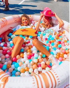 two women sitting in an inflatable pool filled with balloons