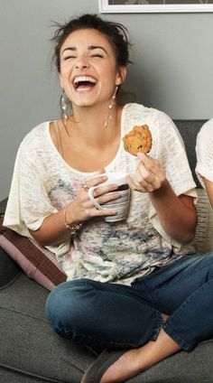 a woman sitting on a couch holding a cup and cookie