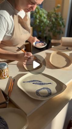 a woman is painting on a plate with paintbrushes