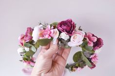 a hand holding a bunch of flowers in front of a white wall with pink and green leaves