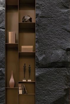 a book shelf with books and vases on it in front of a stone wall